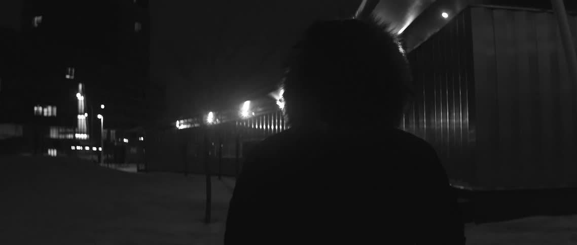 A person wearing a hooded winter coat walking in the city at night