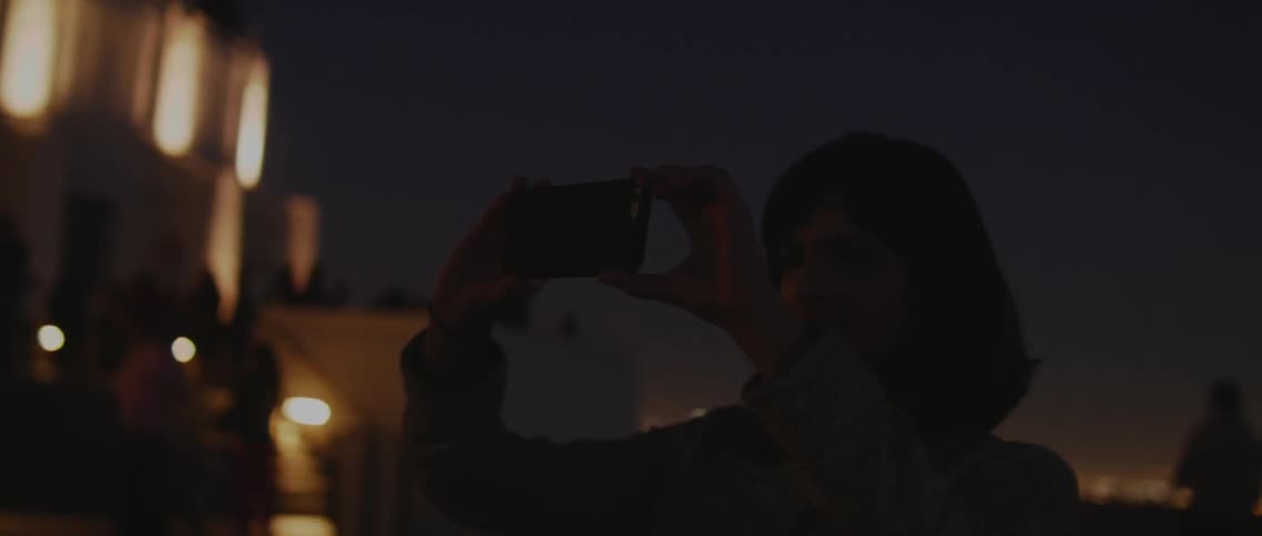 Woman takes a picture on her phone on a street at night