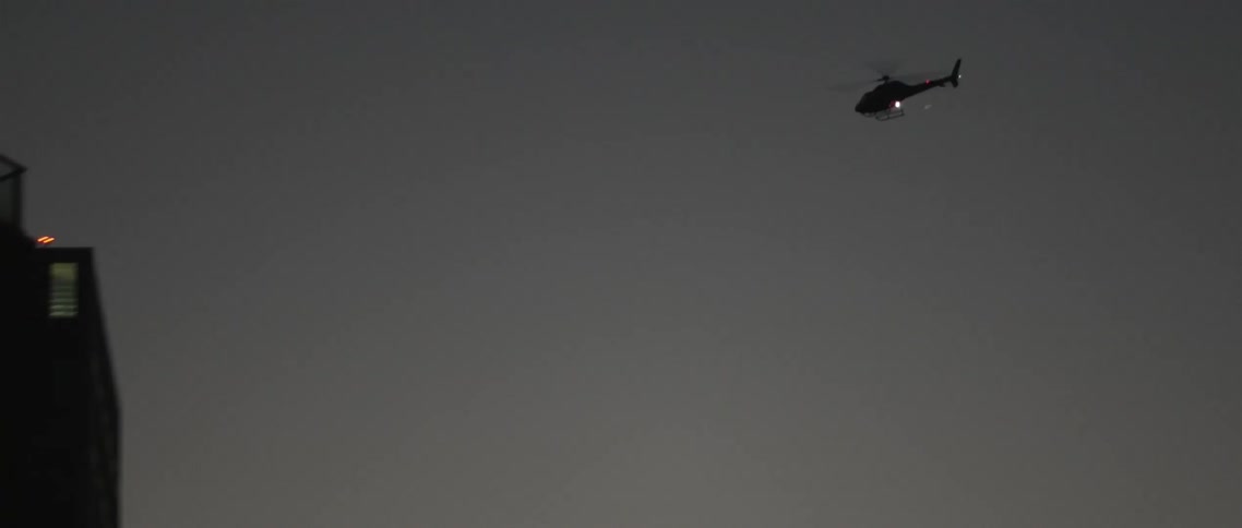A helicopter flies past a building at dusk
