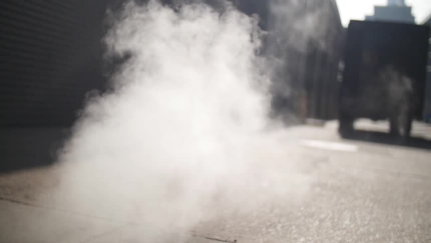 Steam rises from the sewer lid on the city sidewalk