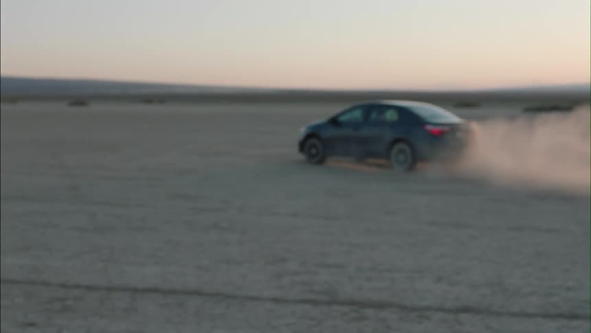 A young woman walks in the desert while a car drives by kicking up dust at sunset