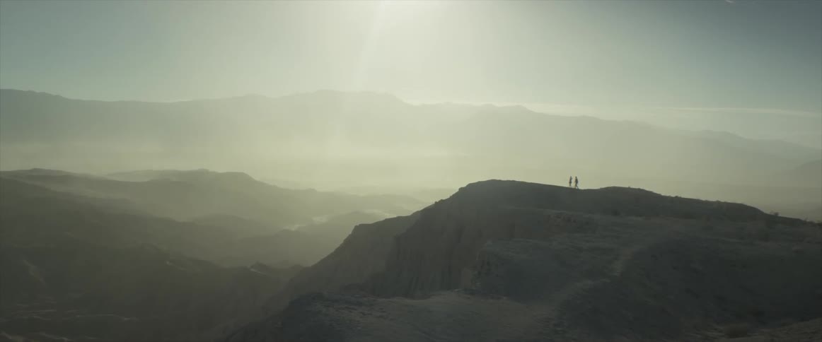 Aerial view of two people walking on top of a mountain