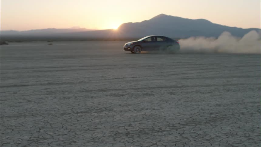 A car drives in a circle on the desert sand, kicking up dust