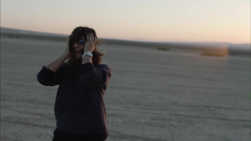 Woman laughing on a windy beach at sunset