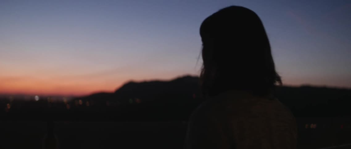 A woman walks toward the railing and looks out at the sunset