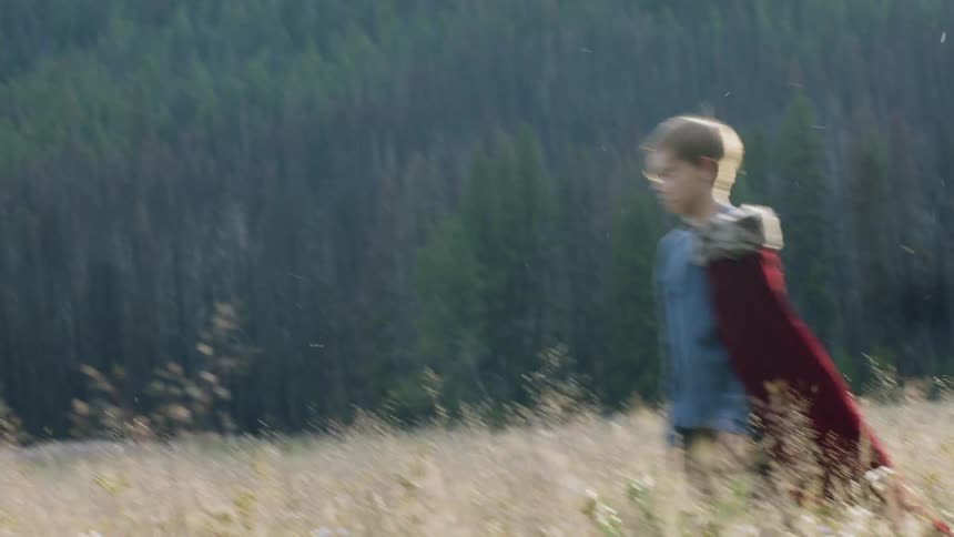 Child wearing a red cape walks through a large field