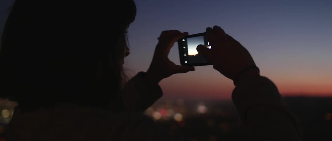 A woman snapping a picture of a city on the horizon