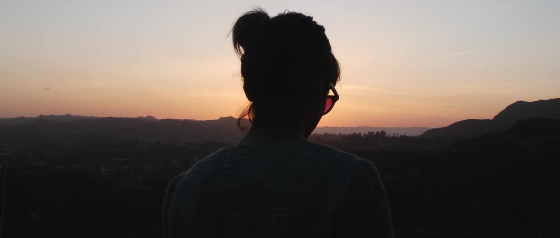 Woman wearing sunglasses looks at the sun setting