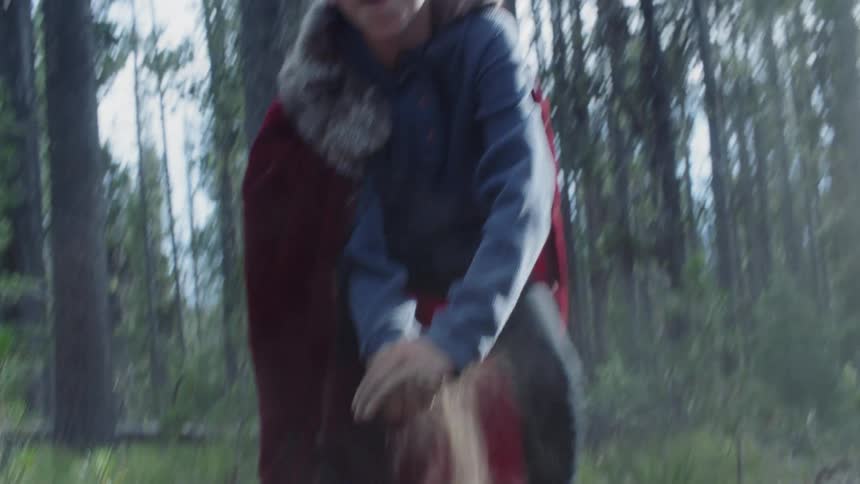 Boy in a red cape picks up dirt and throws it