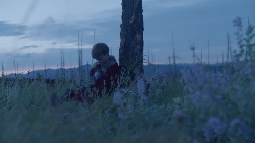 A child wearing a cape sits down in the field