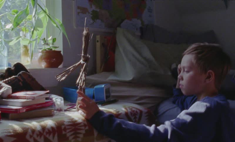 Child sits in his bedroom holding and looking at a stick