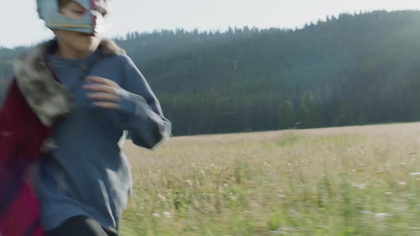Young boy wearing a mask and a cape runs through a field