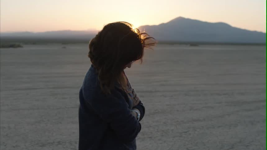 Woman walking on a barren windy field at sunrise