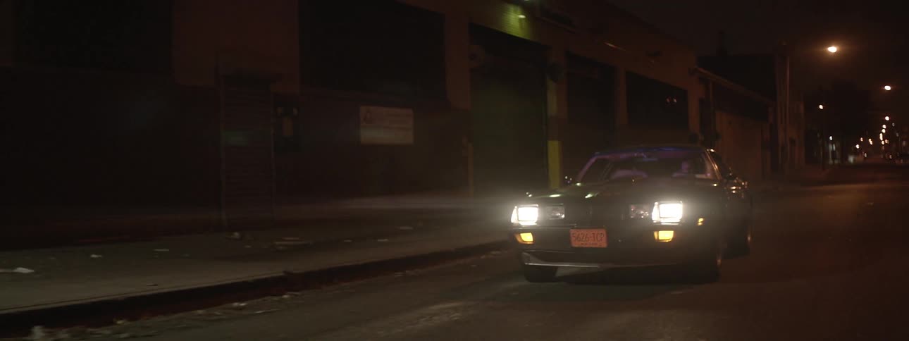 A muscle car drives down the deserted city street at night