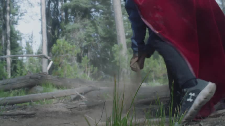 Young boy wearing a red cape picks up dirt and throws it