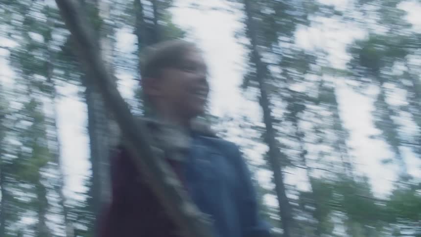 Child wearing a cape and waving a stick in the woods