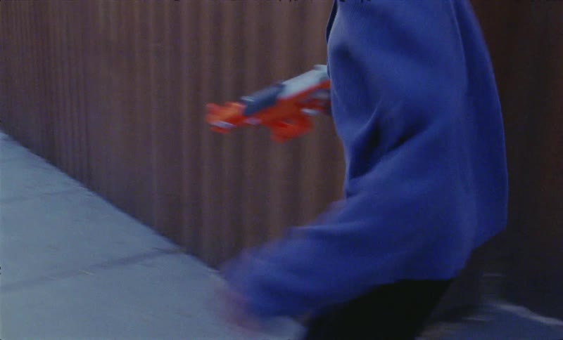 A boy runs through the neighborhood shooting a toy gun