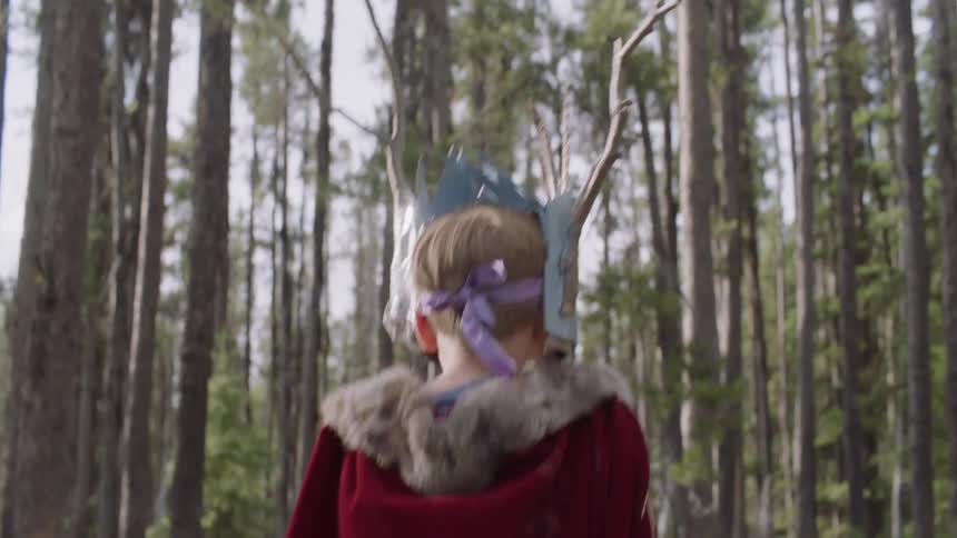 Child wearing a mask and red cape tosses an object and catches it