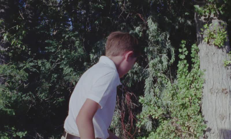 Boy unbuttons his shirt collar and takes off his backpack outside