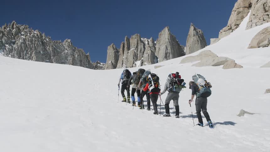 Group of people hike up a snowy mountain on a sunny day