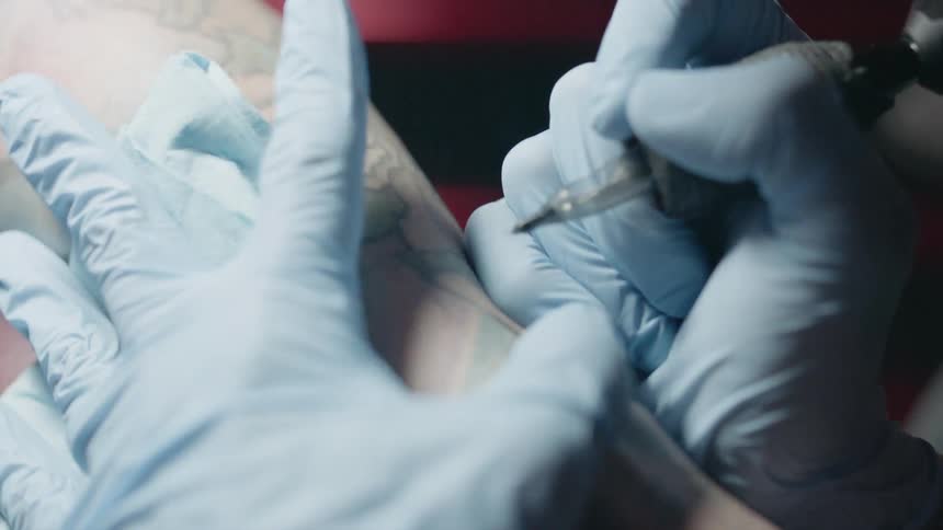 Person wearing gloves tattoos a person's forearm