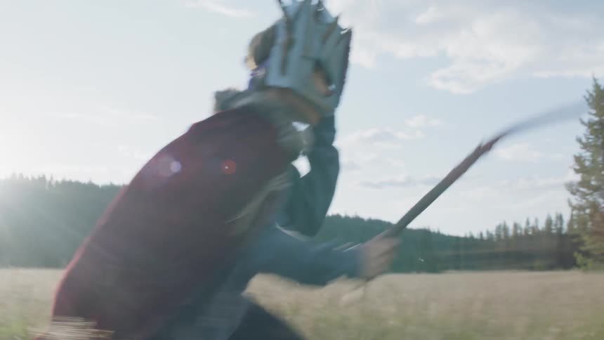 Child dressed as a gladiator runs in a field carrying a stick