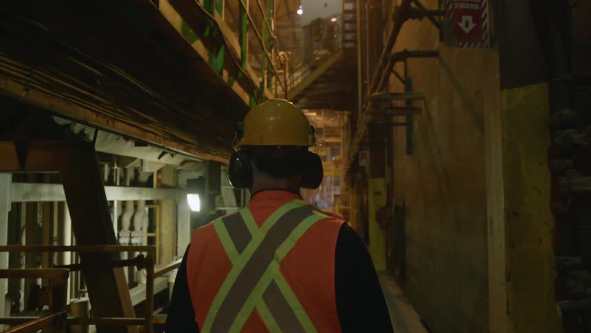 Man wearing a hard hat walks in a dimly lit factory