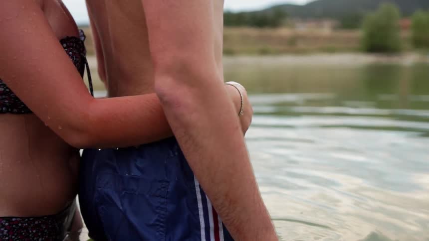 Man and woman stand in a lake together and woman puts her arms around man