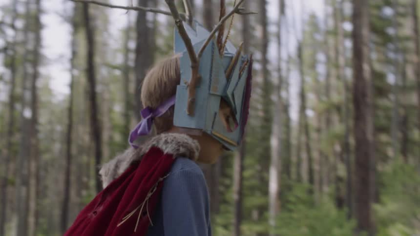 Young boy wearing a mask and cape walks through the forest