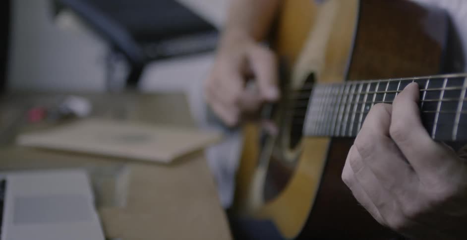 Man plays a guitar then touches the touchpad on a laptop
