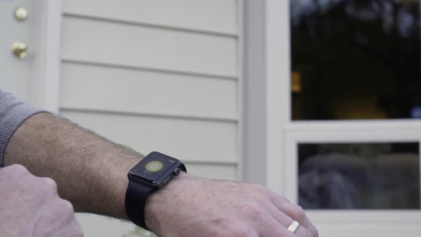 A man is setting on the front porch of a house using a smartwatch in daylight