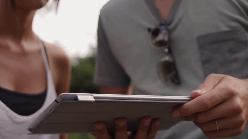 A man and woman use a tablet outside
