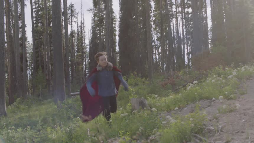 A child wearing a red cape runs from the forest