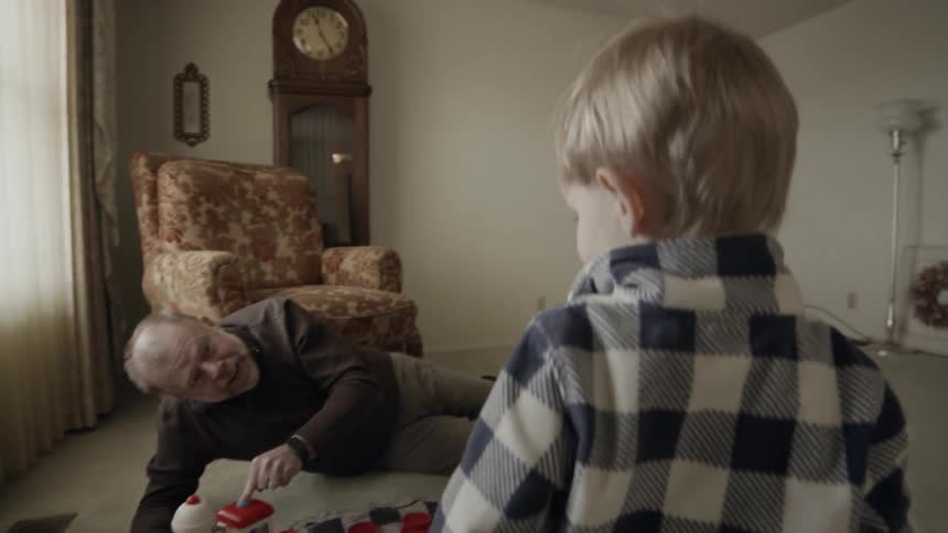 A grandpa is playing with his grandson in a living room in daylight