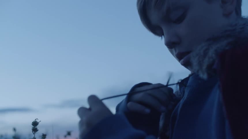 Child unties a cape from his neck and covers up with it outside in the evening