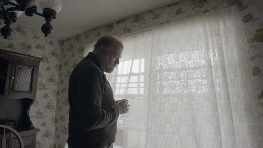 Man stands in front of a window with curtains