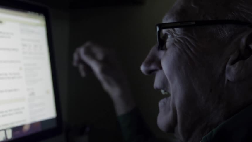 Elderly man talks as he looks at a computer monitor
