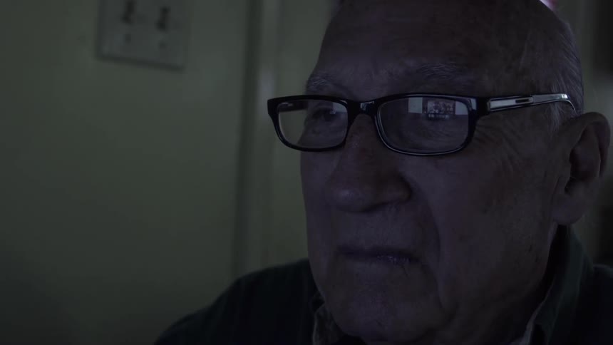 An old man is watching a television inside a home at dusk