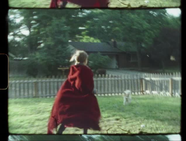 Child wearing a red cape runs through a backyard