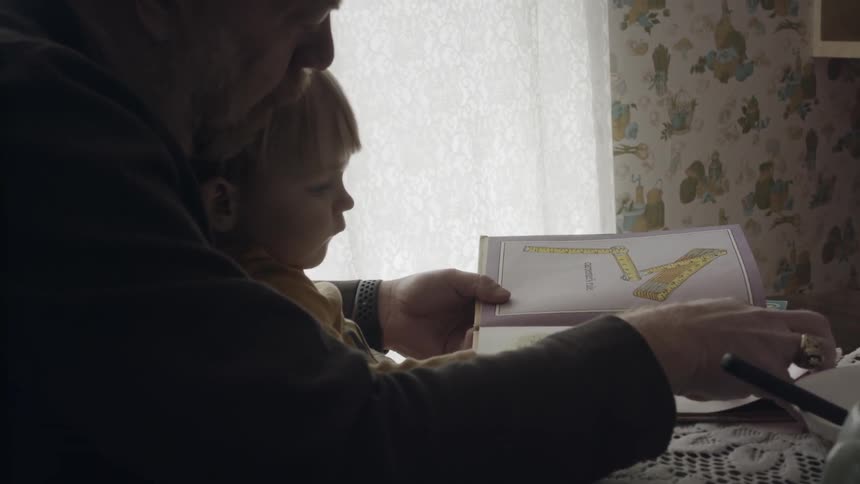 A man holds his grandson in his lap and reads a book with him