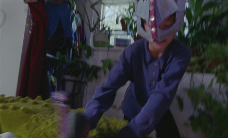 Young boy wearing a mask plays with a toy dinosaur in a bedroom