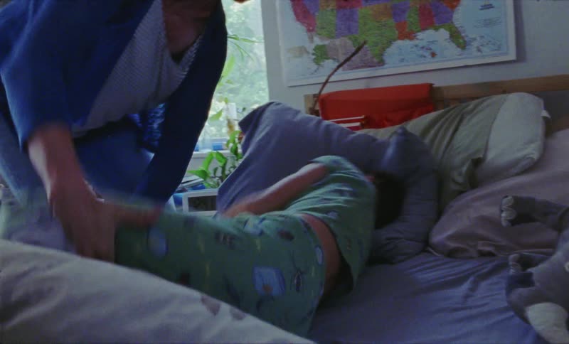 A woman wakes up a boy and pulls him out of bed