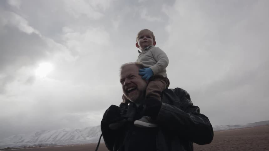 An old man is carrying a toddler on his shoulders outside on a stormy day