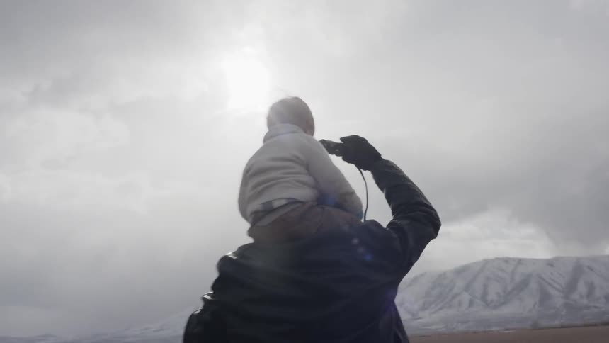 A man holds a boy on his shoulders and holds up binoculars so he can see the hills