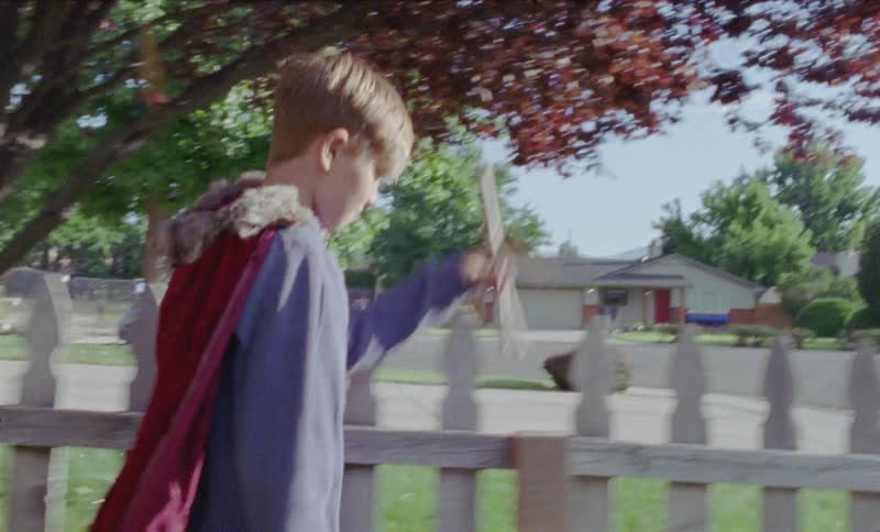 Boy in a costume plays with sticks in a yard
