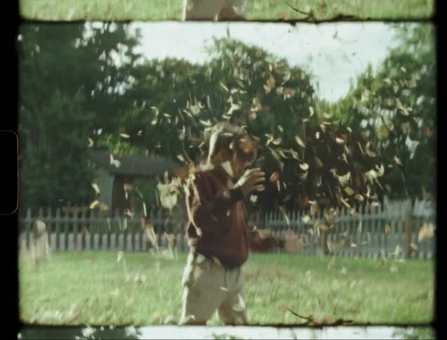 Boy plays with leaves in a front yard