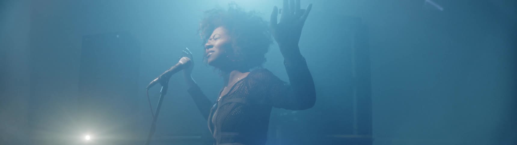 A woman is lifting her arms as she sings on a stage