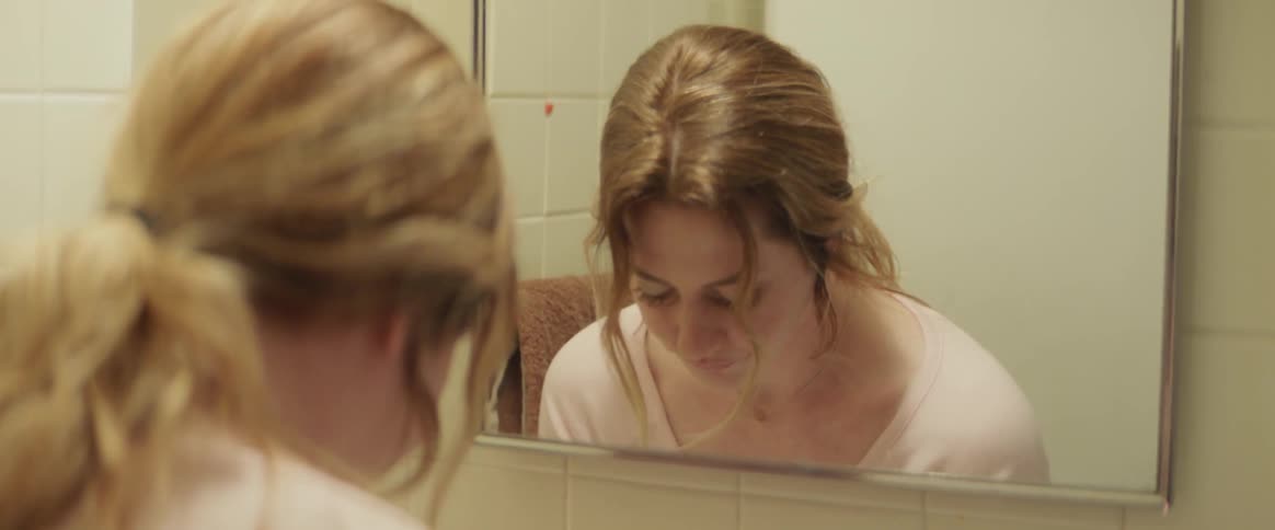 Woman looks in a bathroom mirror and washes her hands