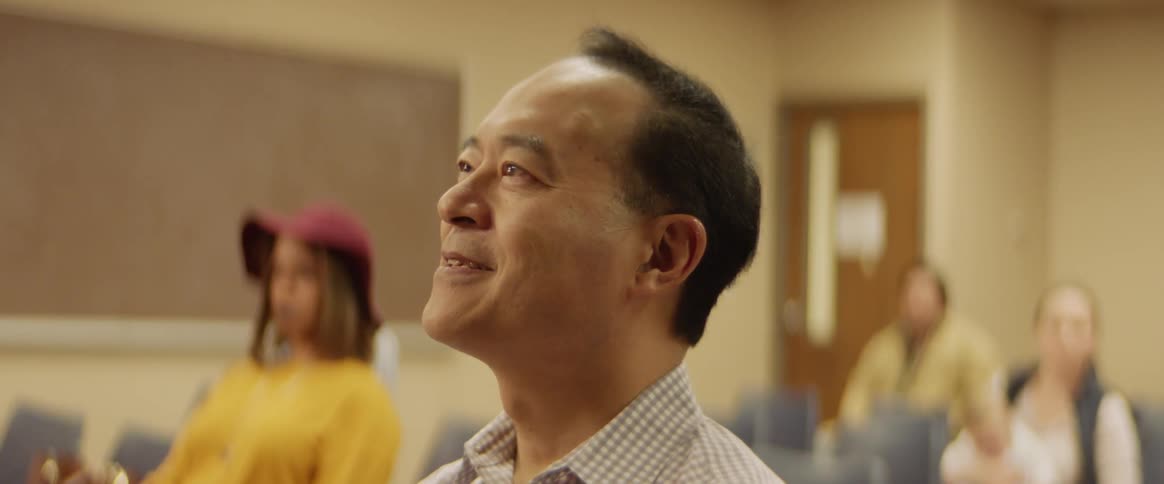 Man smiles while sitting in a room with other people