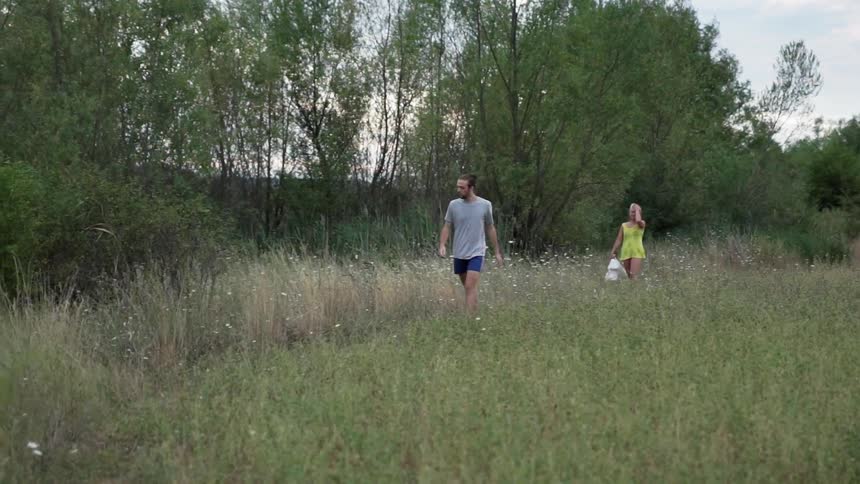 Man and woman walk in a grassy field near trees